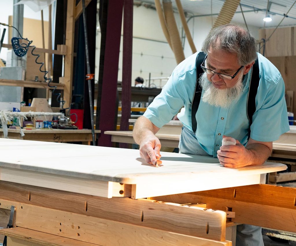 Craftsman finishing a tabletop in a solid wood vs. veneers comparison.