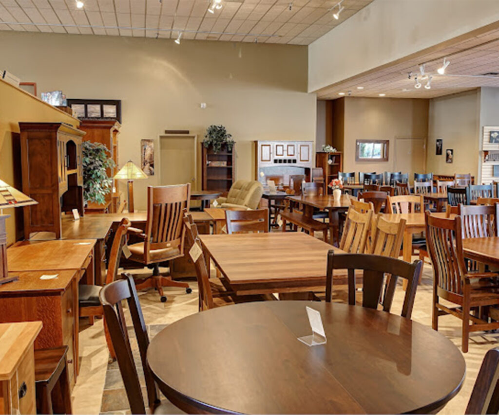 Solid wood furniture showroom with dining tables, chairs, desks, and cabinets on display.