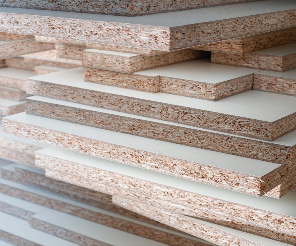 Stacked particleboard panels with white laminate surfaces in a furniture manufacturing setting.