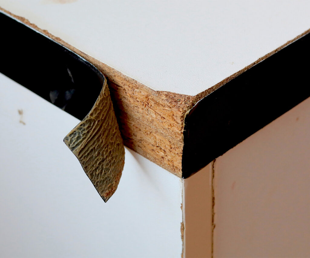 Peeling edge banding exposing particleboard core on a laminated furniture panel.