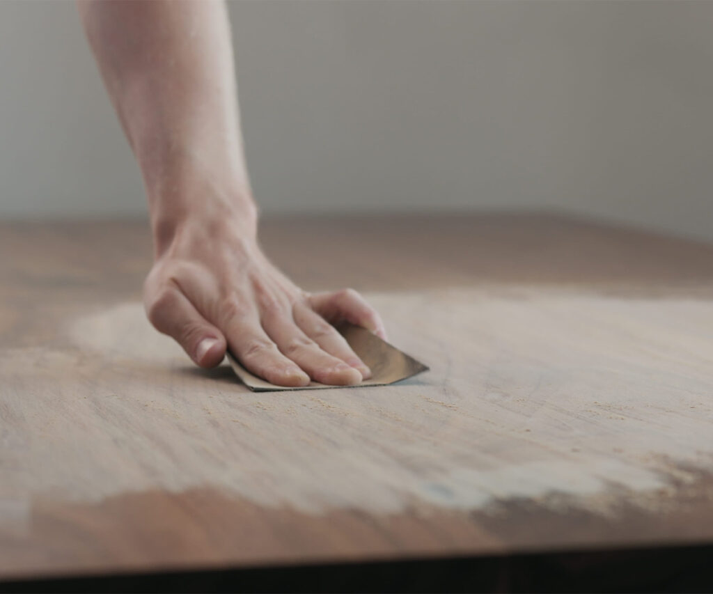 Hand sanding a wood tabletop surface during furniture finishing.
