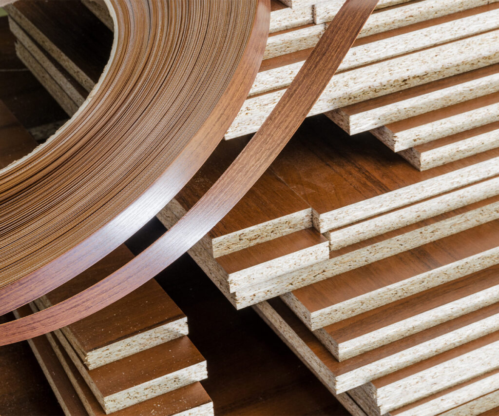 Wood veneer edging roll beside stacked laminated furniture panels.