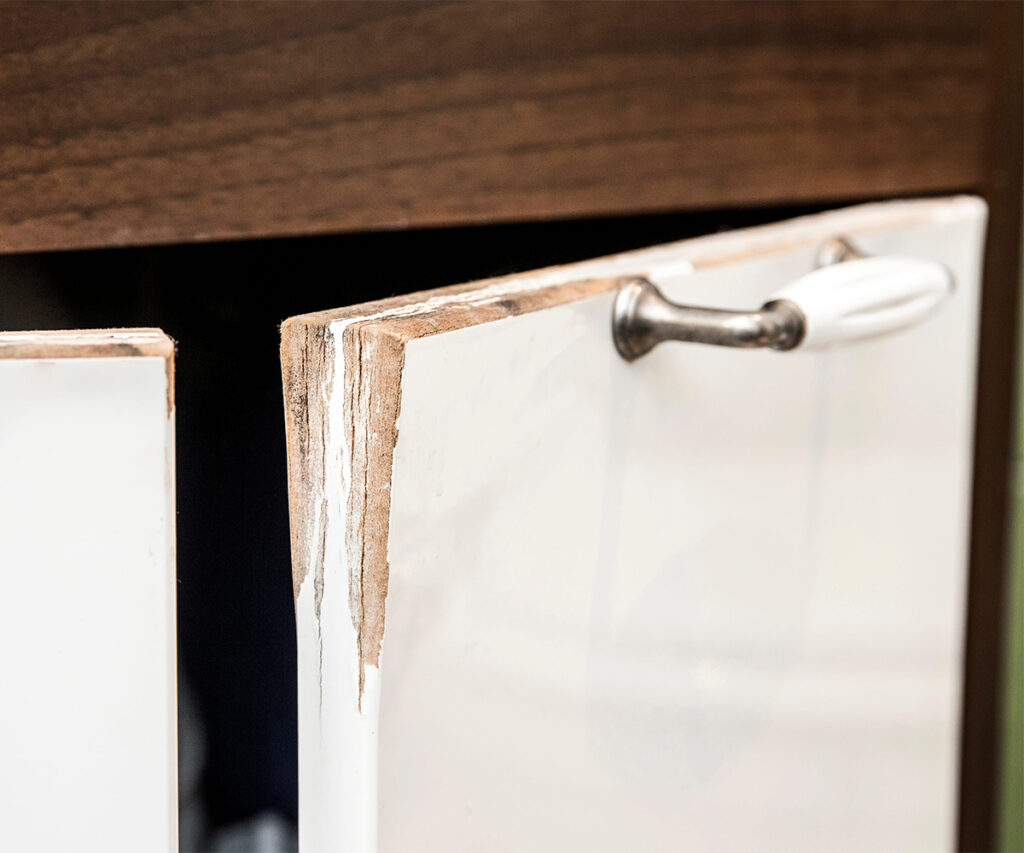 Chipped particleboard cabinet door with peeling white laminate and damaged edge.